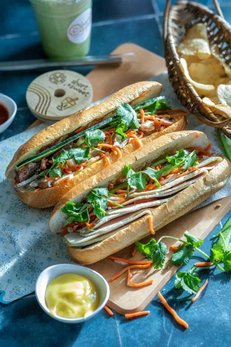 Những ổ bánh mì kẹp thịt, rau và đồ chua bên chén sốt