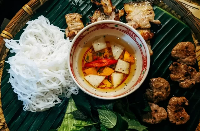 Đĩa bún với thịt nướng, rau thơm và nước chấm trên lá chuối (ảnh gần giống cao lầu)