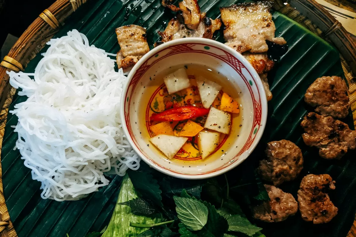 Đĩa bún với thịt nướng, rau thơm và nước chấm trên lá chuối (ảnh gần giống cao lầu)