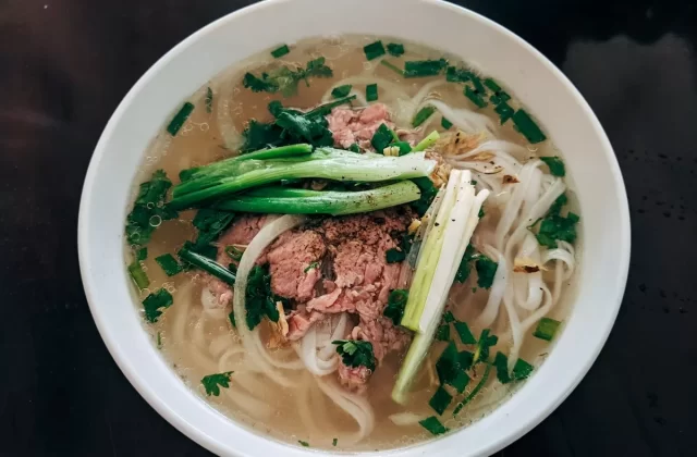 Tô phở bò với thịt, hành lá và rau thơm trong bát sứ trắng