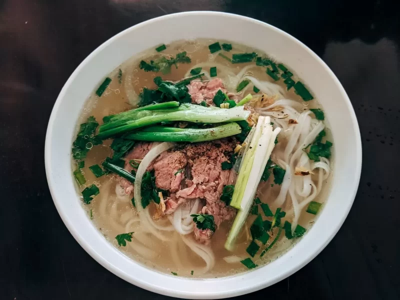 Tô phở bò với thịt, hành lá và rau thơm trong bát sứ trắng