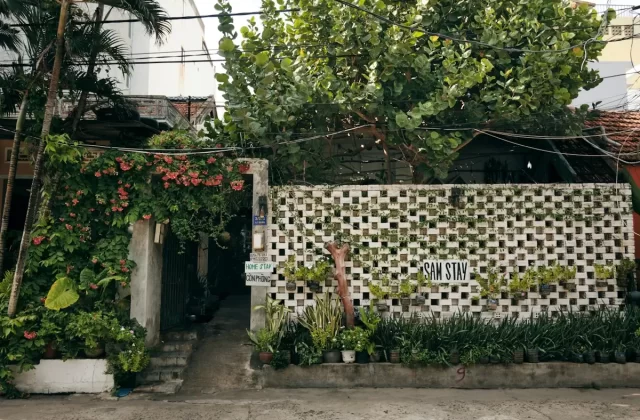 Lối vào homestay với tường gạch thông gió trắng và cây xanh