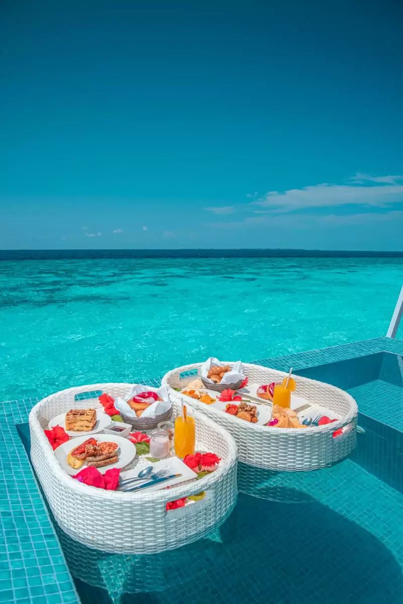 Hai khay bữa sáng nổi trên hồ bơi nước xanh tại biệt thự Maldives