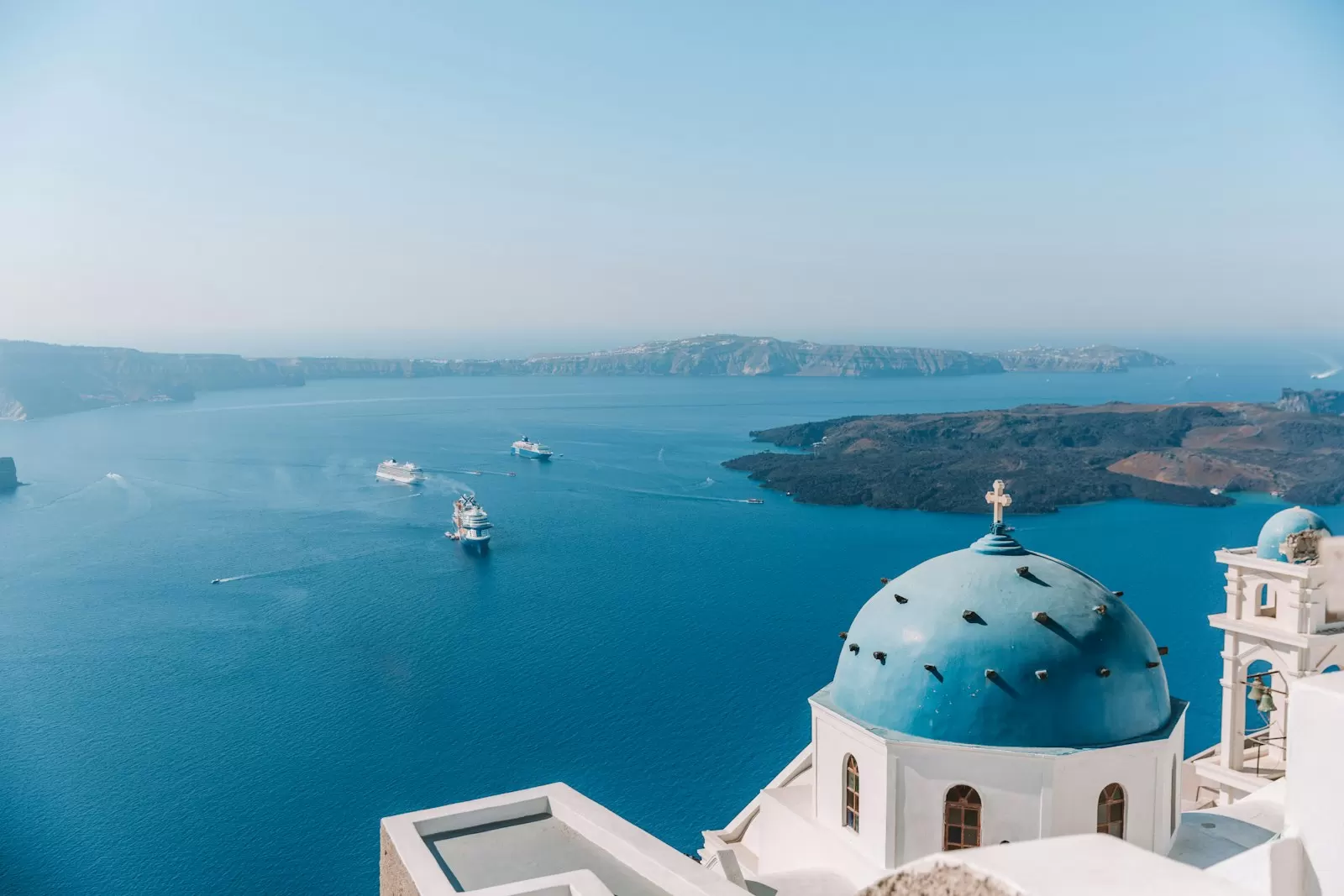 Nhà thờ mái vòm xanh nhìn ra biển Aegean từ sườn caldera Santorini