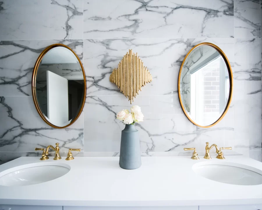 Phòng tắm ốp đá marble vân xám với hai bồn rửa và gương tròn viền vàng