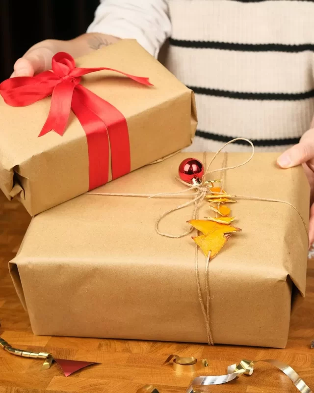 Đôi tay trao hai hộp quà gói giấy kraft, một hộp thắt nơ đỏ