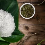 Nắm gạo nếp trắng đặt trên lá dong xanh cạnh chén đậu xanh trên bàn gỗ