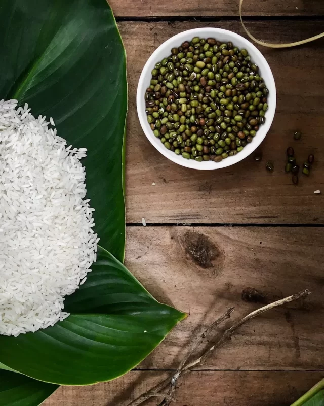 Nắm gạo nếp trắng đặt trên lá dong xanh cạnh chén đậu xanh trên bàn gỗ