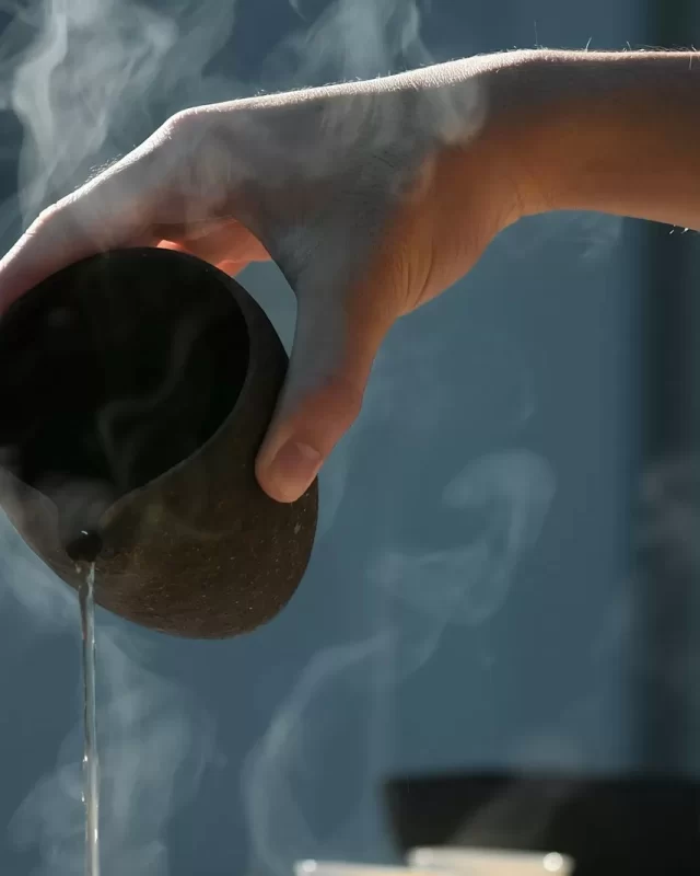 Bàn tay rót nước nóng bốc hơi từ chiếc bình gốm sẫm màu