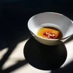 Chén sứ trắng đựng nước mắm màu hổ phách với ớt đỏ thái lát, nắng chiếu nghiêng