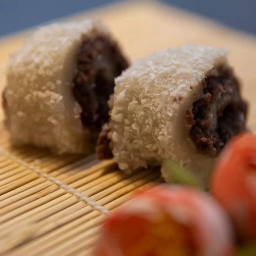 Hai miếng bánh cuộn phủ dừa, nhân sẫm màu đặt trên mành tre