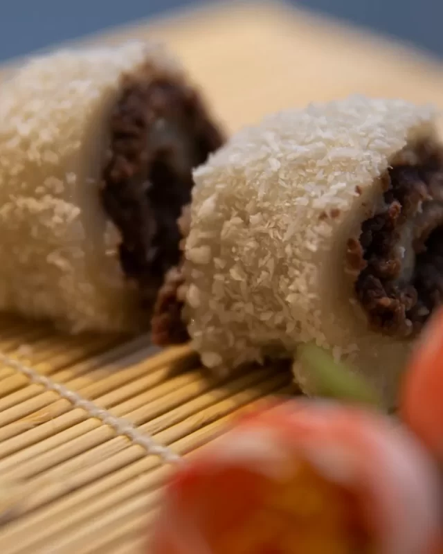 Hai miếng bánh cuộn phủ dừa, nhân sẫm màu đặt trên mành tre