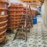 Dãy thùng gỗ lớn ủ nước mắm đai dây thừng trong nhà thùng, có thang gỗ dựng bên