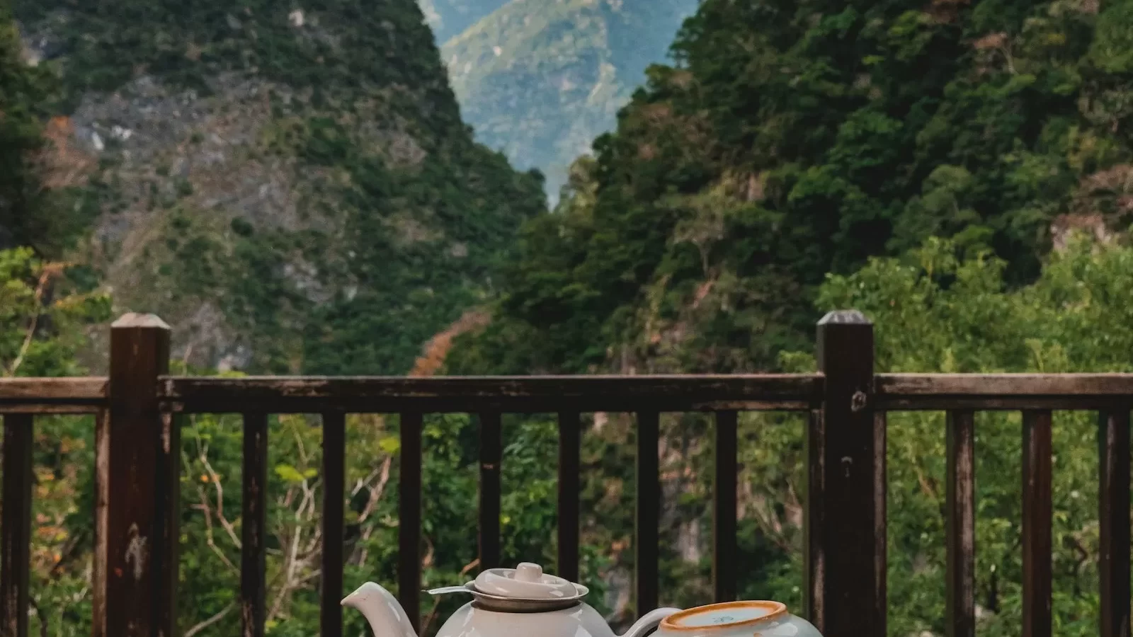 Ấm trà trên ban công gỗ nhìn ra núi đá xanh thẫm và thung lũng