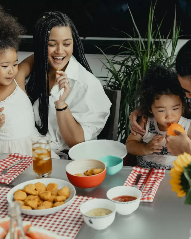 Cả nhà cười vui bên bàn ăn bày nhiều món, có bình hoa hướng dương
