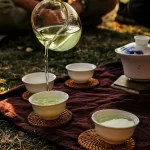 Rót trà xanh từ bình thủy tinh vào những chén sứ trắng trên tấm vải
