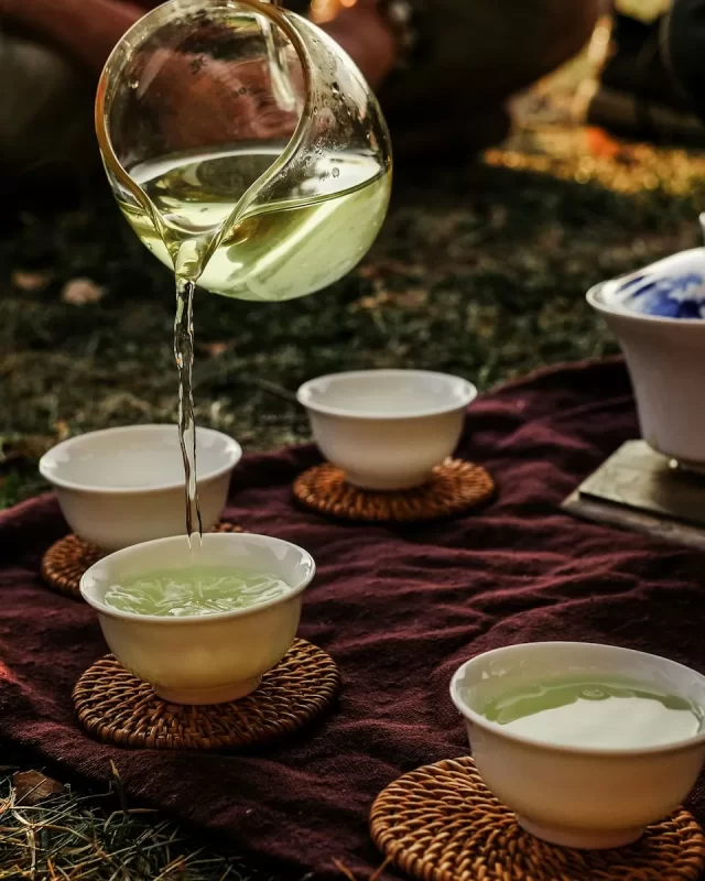 Rót trà xanh từ bình thủy tinh vào những chén sứ trắng trên tấm vải