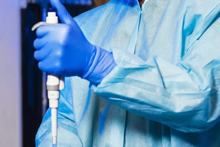 Chuyên viên mặc áo choàng xanh dùng pipet trong phòng thí nghiệm