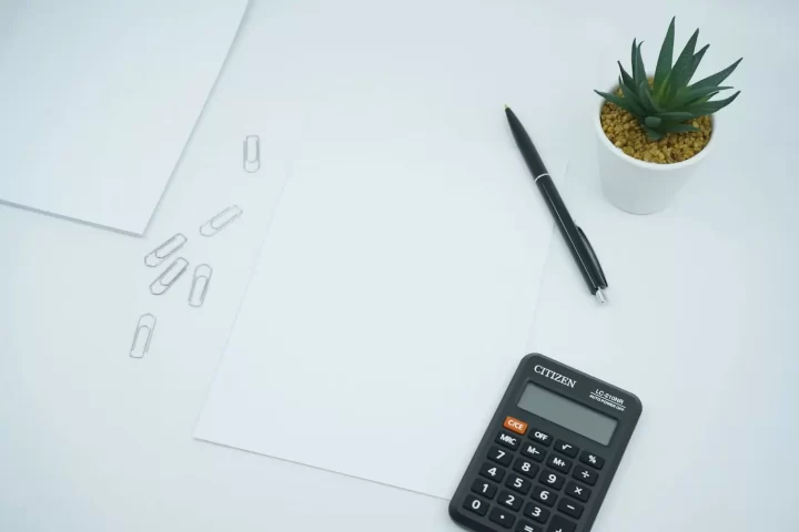 Máy tính bỏ túi và bút đặt trên tờ giấy trắng