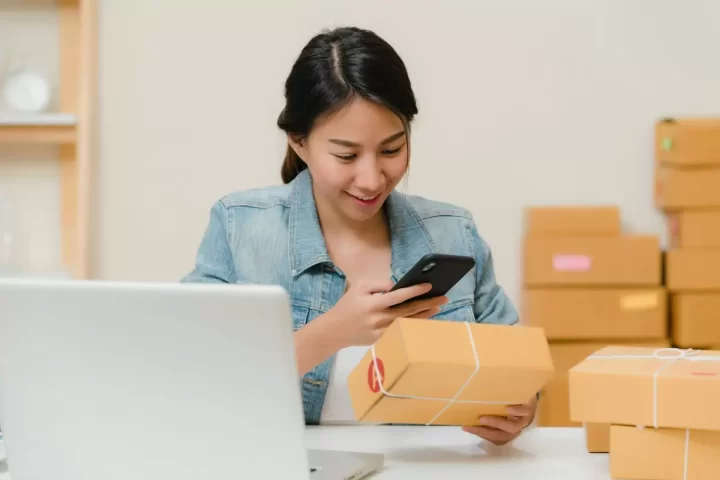 Người bán hàng online kiểm tra đơn hàng bên laptop và thùng hàng