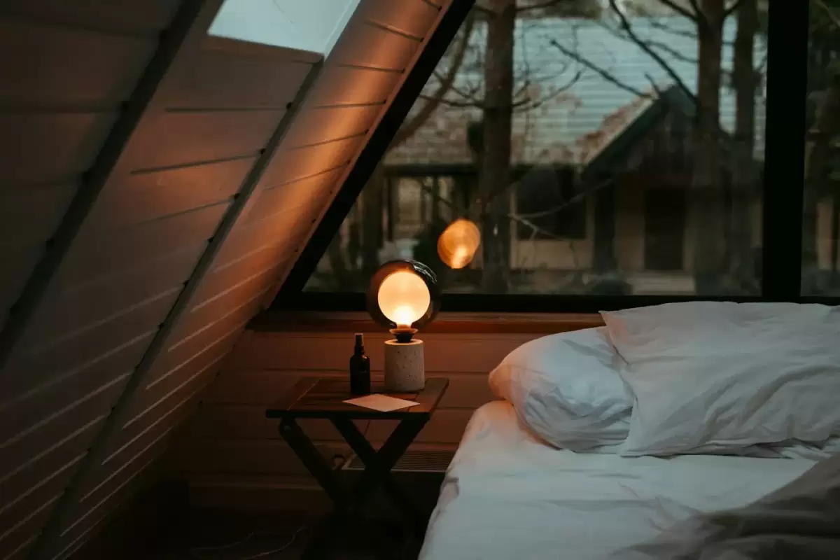 Phòng gác mái gỗ ấm với đèn bàn và giường thấp, kiểu phòng nghỉ nhà sàn tại Du Già Bên Suối