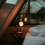 Phòng gác mái gỗ ấm với đèn bàn và giường thấp, kiểu phòng nghỉ nhà sàn tại Du Già Bên Suối