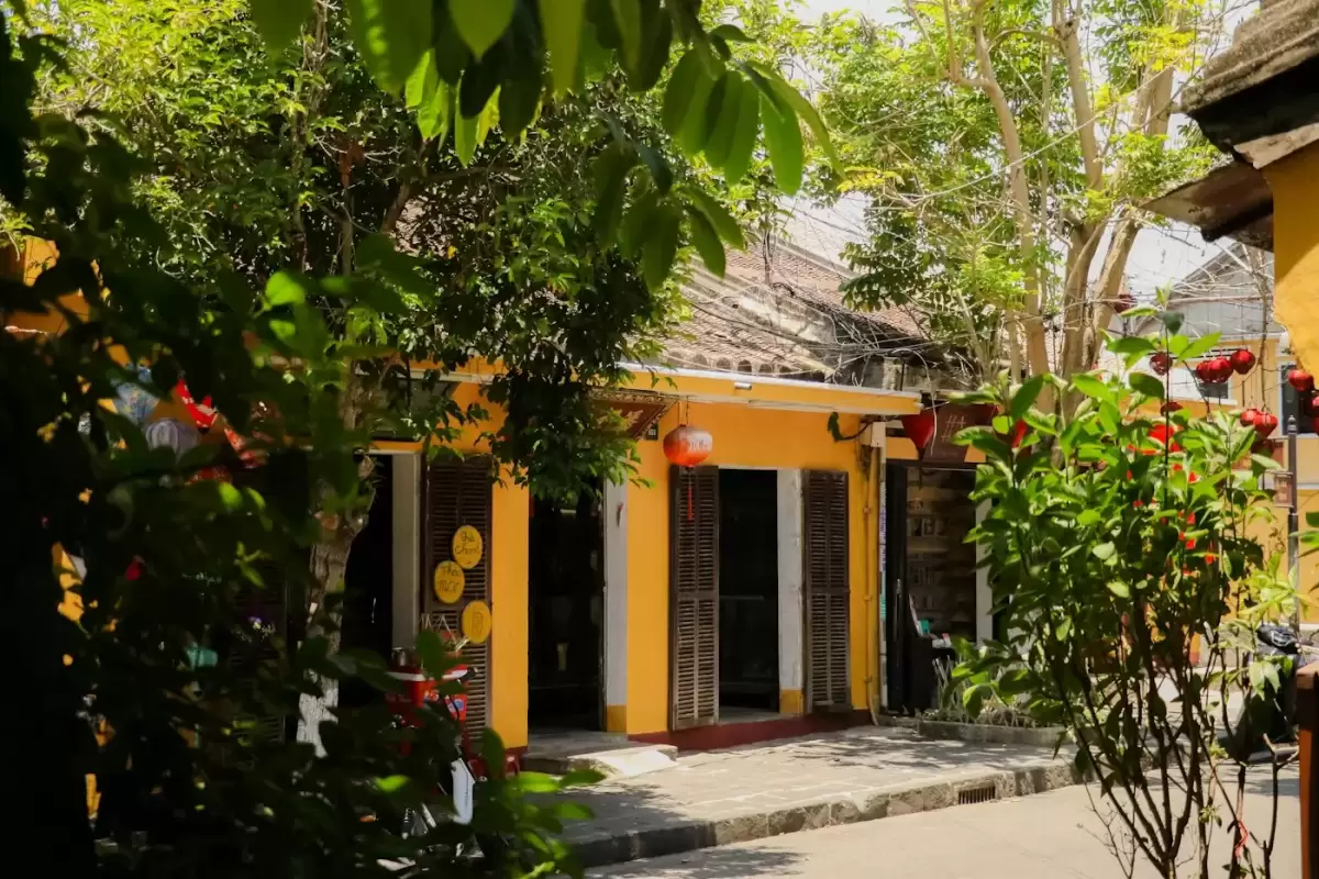 Mặt tiền ngôi nhà vàng có hàng hiên nhỏ và cây xanh trong hẻm Hội An, nơi đặt homestay Góc Nhỏ · Hẻm Cau Lầu