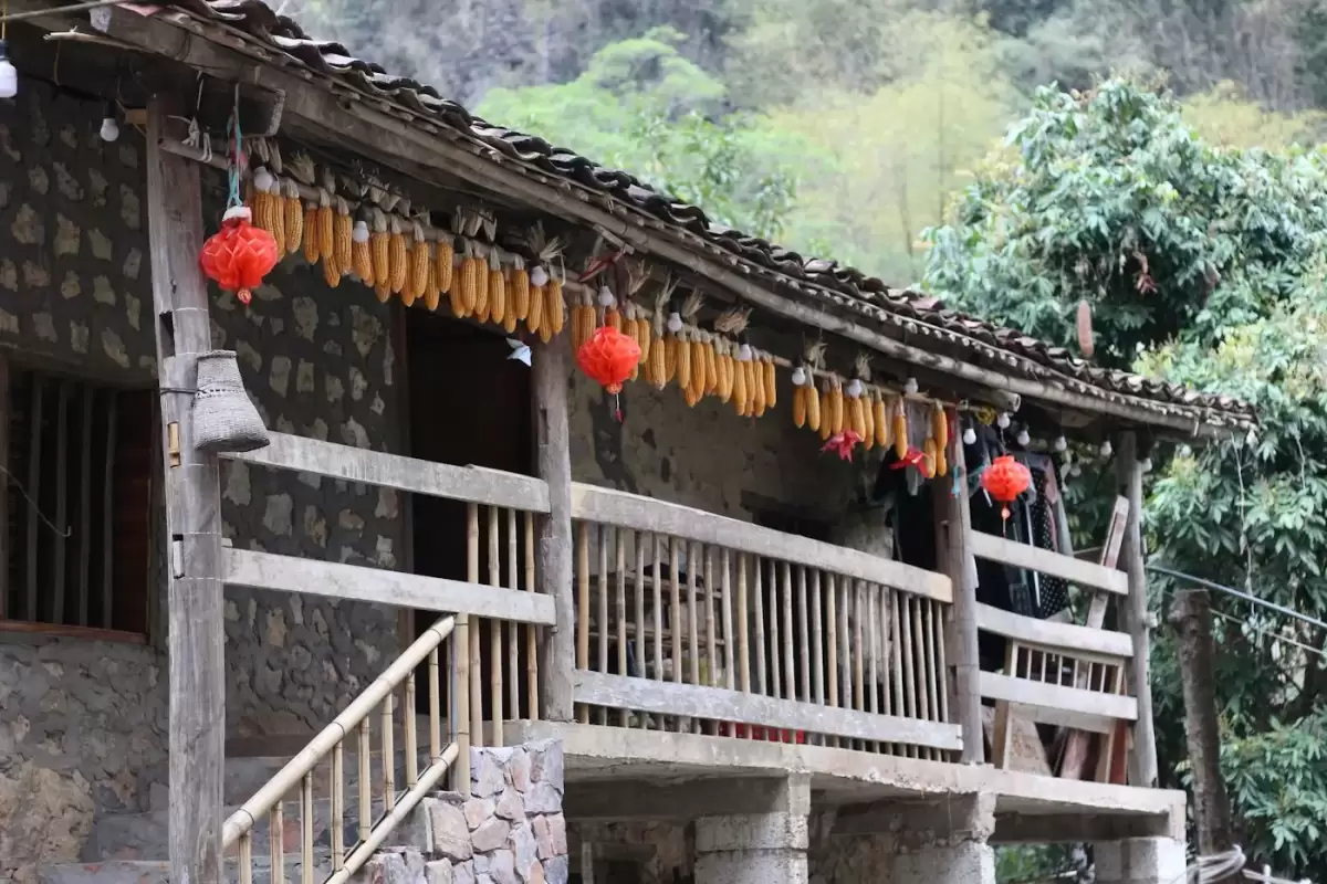 Ngôi nhà gỗ vùng cao treo bắp ngô và đèn lồng đỏ dưới hiên, gợi không khí nhà trình tường ở Đồng Văn, Hà Giang