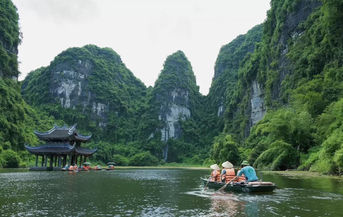 Thuyền khách trên sông giữa núi đá và ngôi chùa nhỏ ở Ninh Bình