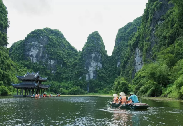 Thuyền khách trên sông giữa núi đá và ngôi chùa nhỏ ở Ninh Bình