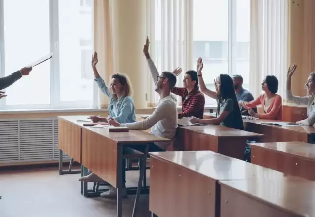Giáo viên đứng lớp nhỏ, học viên giơ tay phát biểu bên cửa sổ sáng