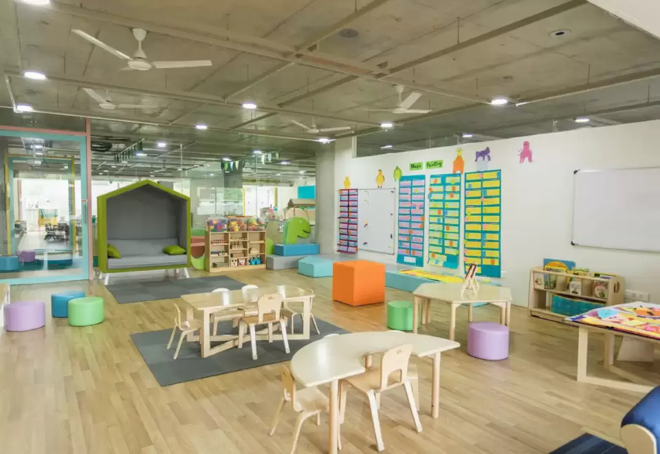 Lớp học Montessori rộng sáng với kệ thấp, bàn ghế nhỏ và góc đọc sách nhìn từ xa