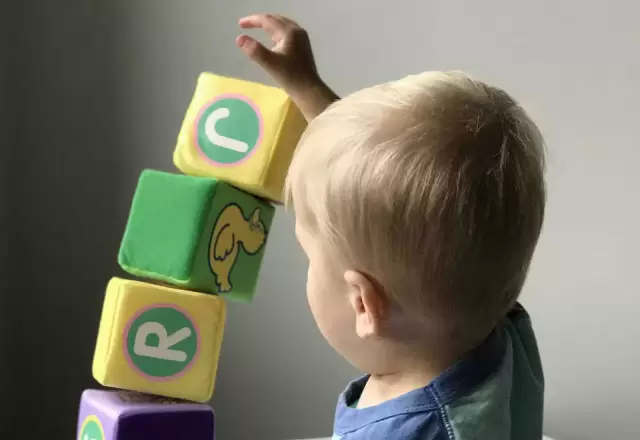 Bé trai xếp chồng những khối gỗ có chữ cái trên bàn trắng, trò chơi Montessori tại nhà