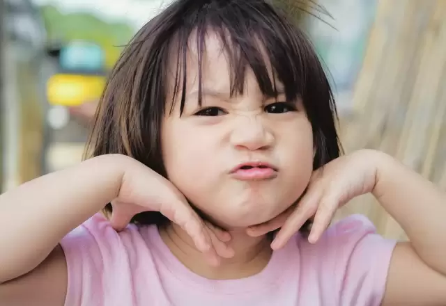 Bé gái chu môi, hai tay chống má làm vẻ mặt bướng bỉnh đáng yêu