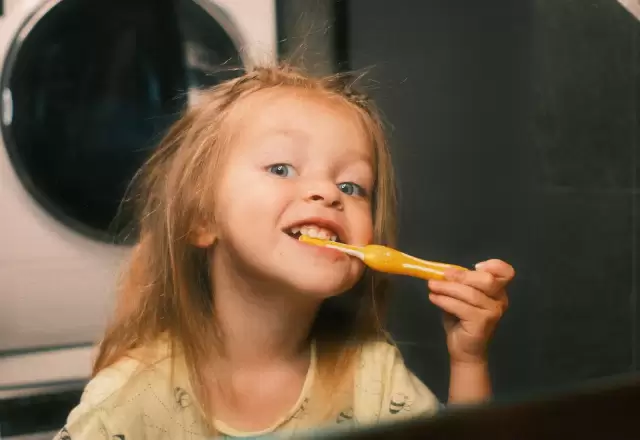 Bé gái vừa đánh răng vừa cười trong phòng tắm, thói quen buổi sáng của bé