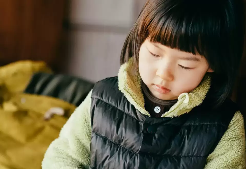 Bé gái tóc mái ngố mặc áo phao đen nhìn xuống chăm chú, chuẩn bị đến lớp