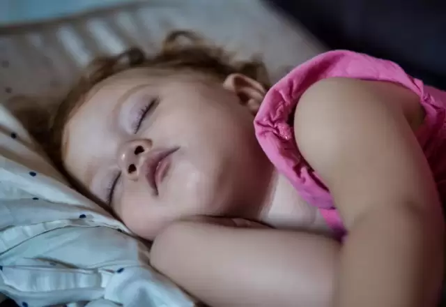 Bé gái nằm ngủ ngon lành trên gối, hai tay khoanh dưới má