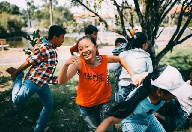 Bé gái cười tươi chạy giữa nhóm bạn trong buổi vui chơi ngoài trời