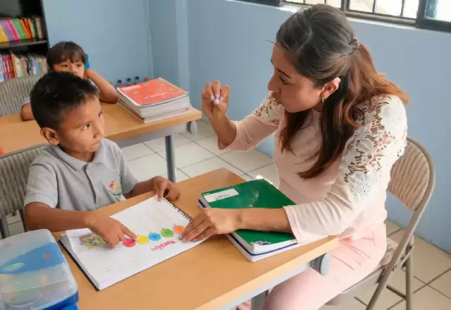 Cô giáo chỉ vào sách bài tập màu sắc, hướng dẫn bé trong buổi sinh hoạt chuyên đề