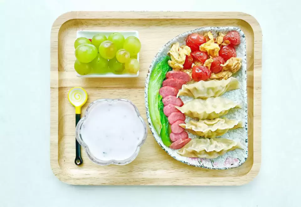 Khay gỗ có nho xanh, sủi cảo, thịt nguội và sữa chua dành cho bữa ăn của bé
