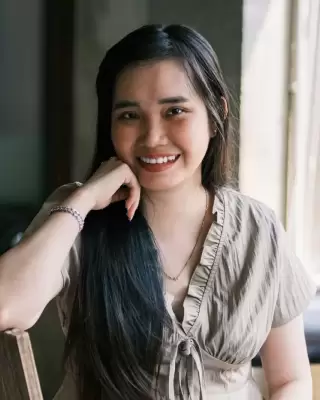 Chị phụ huynh trẻ tóc dài tựa cằm lên tay, mỉm cười bên khung cửa sổ