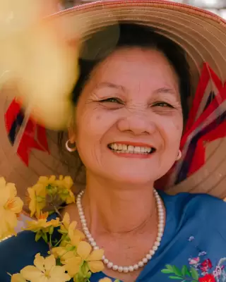 Bà ngoại nón lá cười hiền, đeo chuỗi ngọc trai giữa những bông hoa vàng