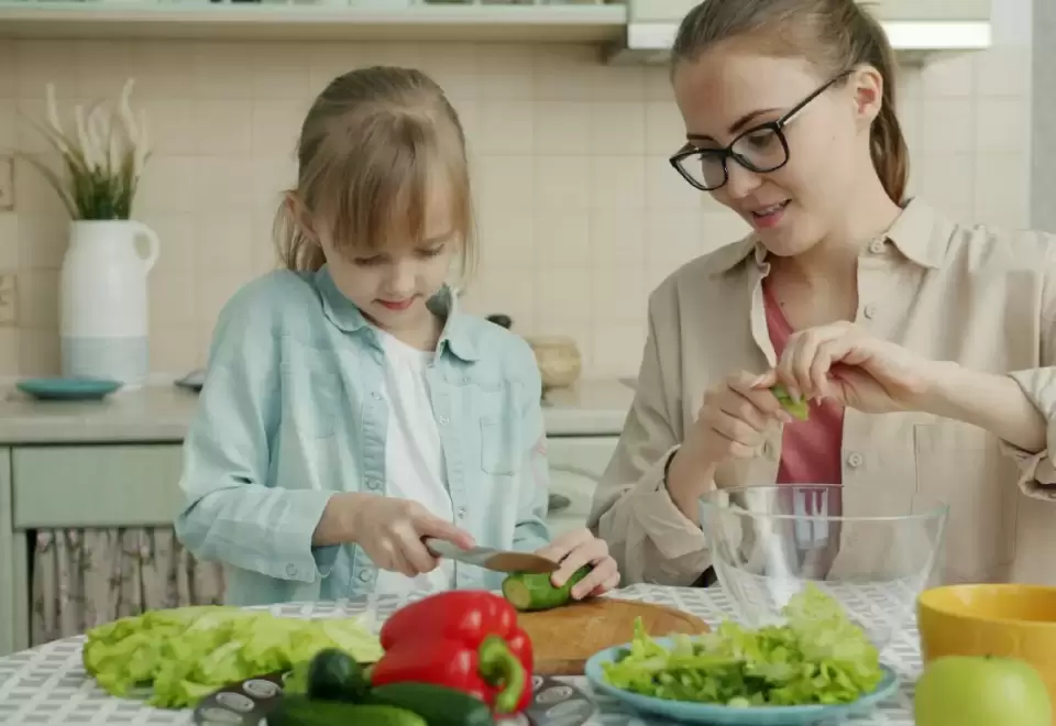 Cô giáo và bé gái cùng cắt rau củ làm món salad trong căn bếp sáng