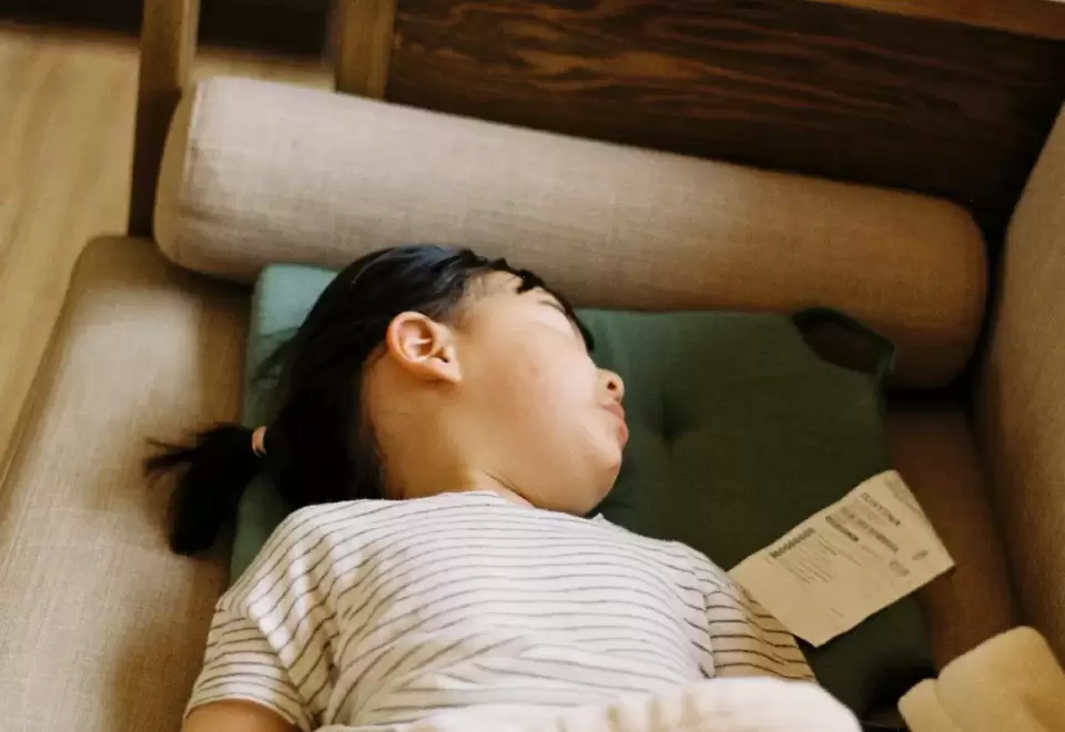 Bé nằm ngủ yên trên giường gỗ với chăn mỏng trong căn phòng ấm áp