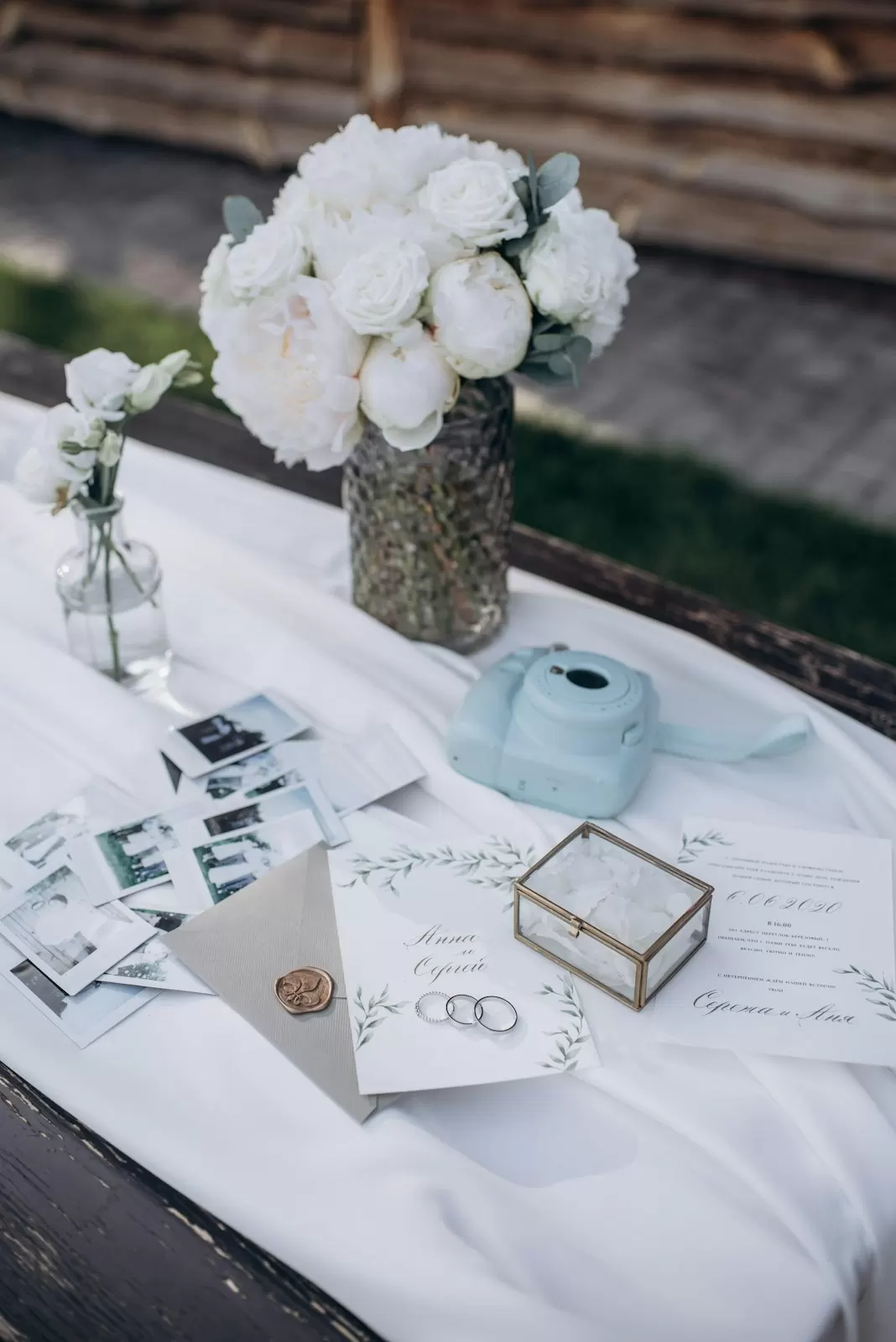 Hộp nhẫn, ảnh polaroid và phong bì đặt cạnh bình hoa mẫu đơn trắng