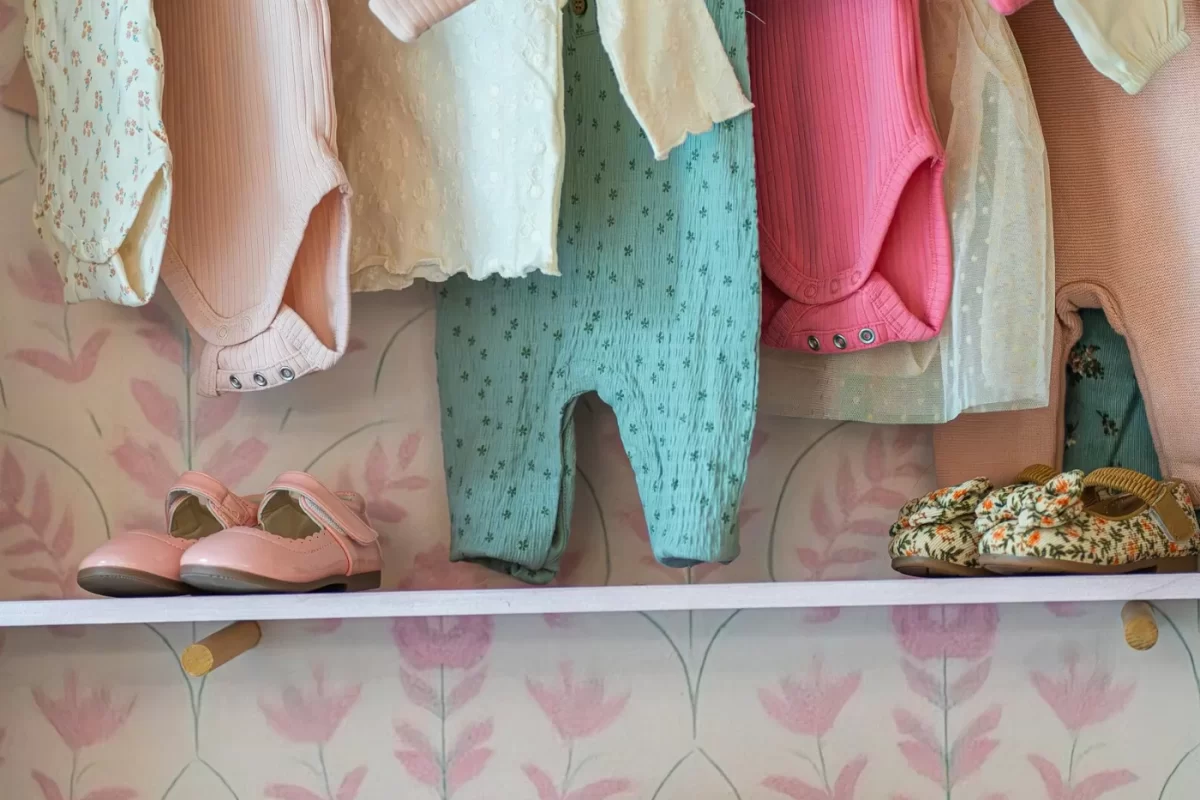 Quần áo sơ sinh màu pastel treo trên giá, bên dưới là giày nhỏ và vali xinh