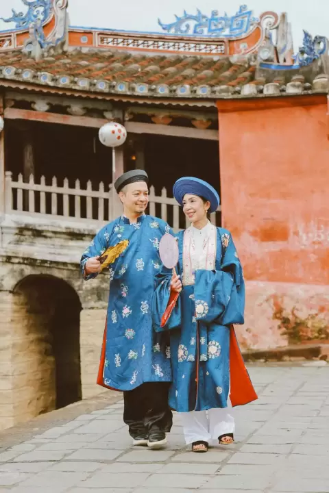 Ảnh cưới Hội An phong cách Cổ điển: cặp đôi áo dài đứng bên nhau trước cây cầu mái ngói
