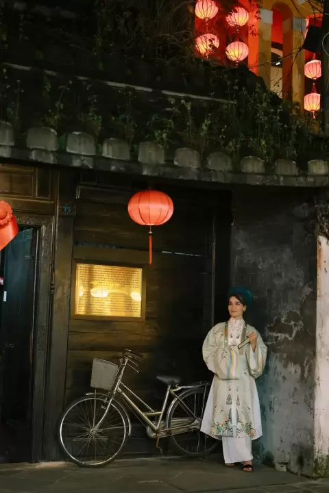 Ảnh cưới Hội An phong cách Cổ điển: cô gái áo dài trắng đứng cạnh chiếc xe đạp dưới đèn lồng đỏ