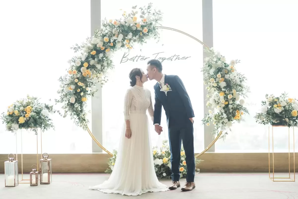 Ảnh cưới Sài Gòn phong cách Hàn Quốc: cô dâu chú rể hôn nhau dưới vòm hoa trắng cạnh cửa sổ lớn