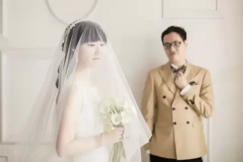 Ảnh cưới Sài Gòn phong cách Hàn Quốc: cô dâu phủ voan mỏng đứng cạnh chú rể vest be trên nền tường sáng